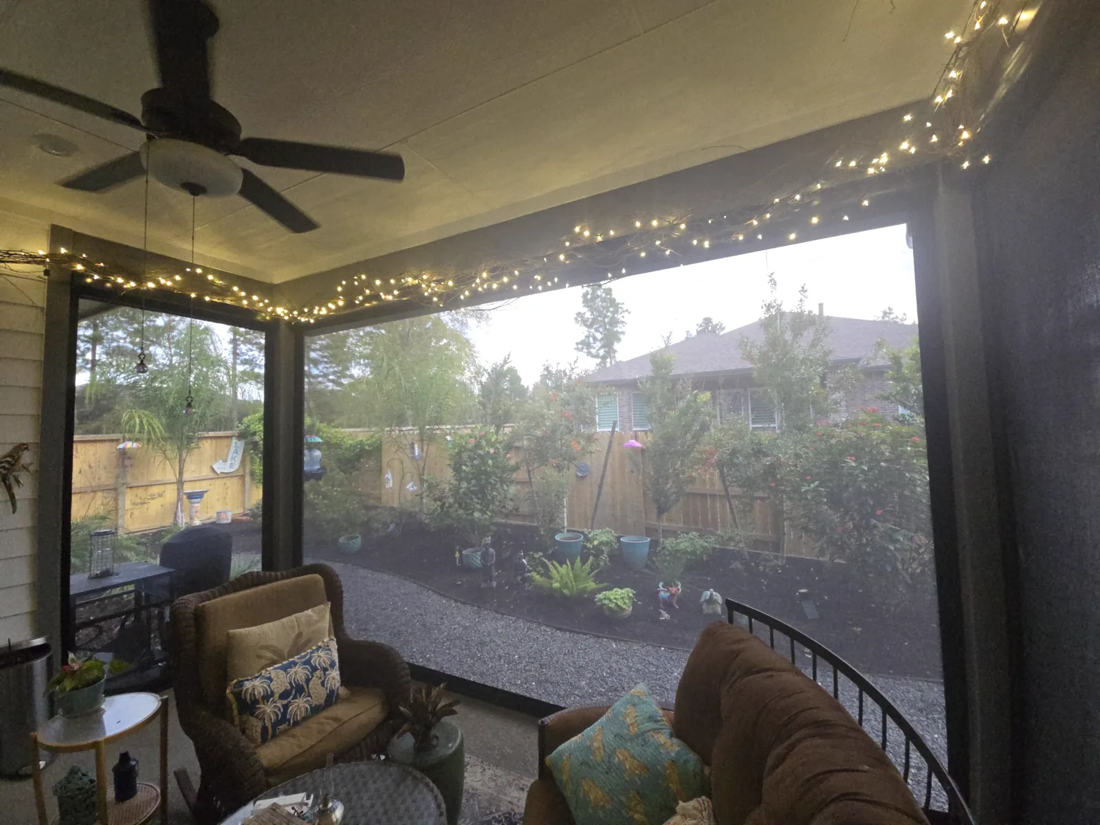 Covered Houston patio strung with warm holiday lights, with cushioned seating and a garden view through the screens.