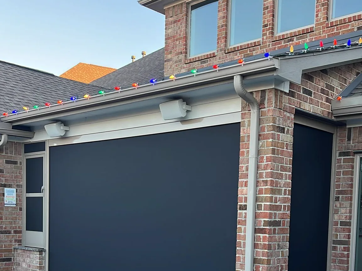 Holiday string lights running along the roofline above motorized patio screens on a Houston home.