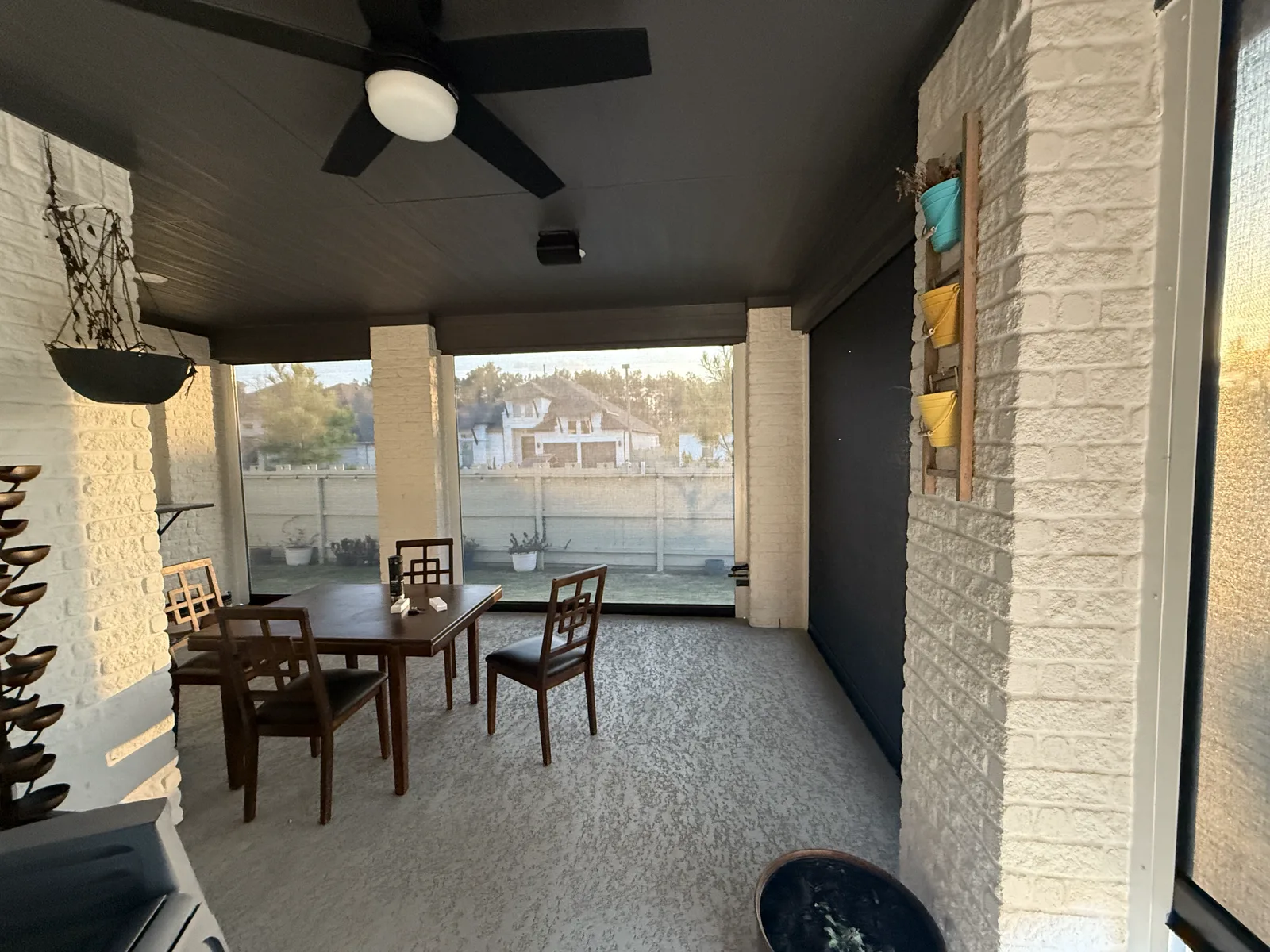 Inside a screened Houston patio set up as a private retreat, with a dining table, ceiling fan, and hanging plants.